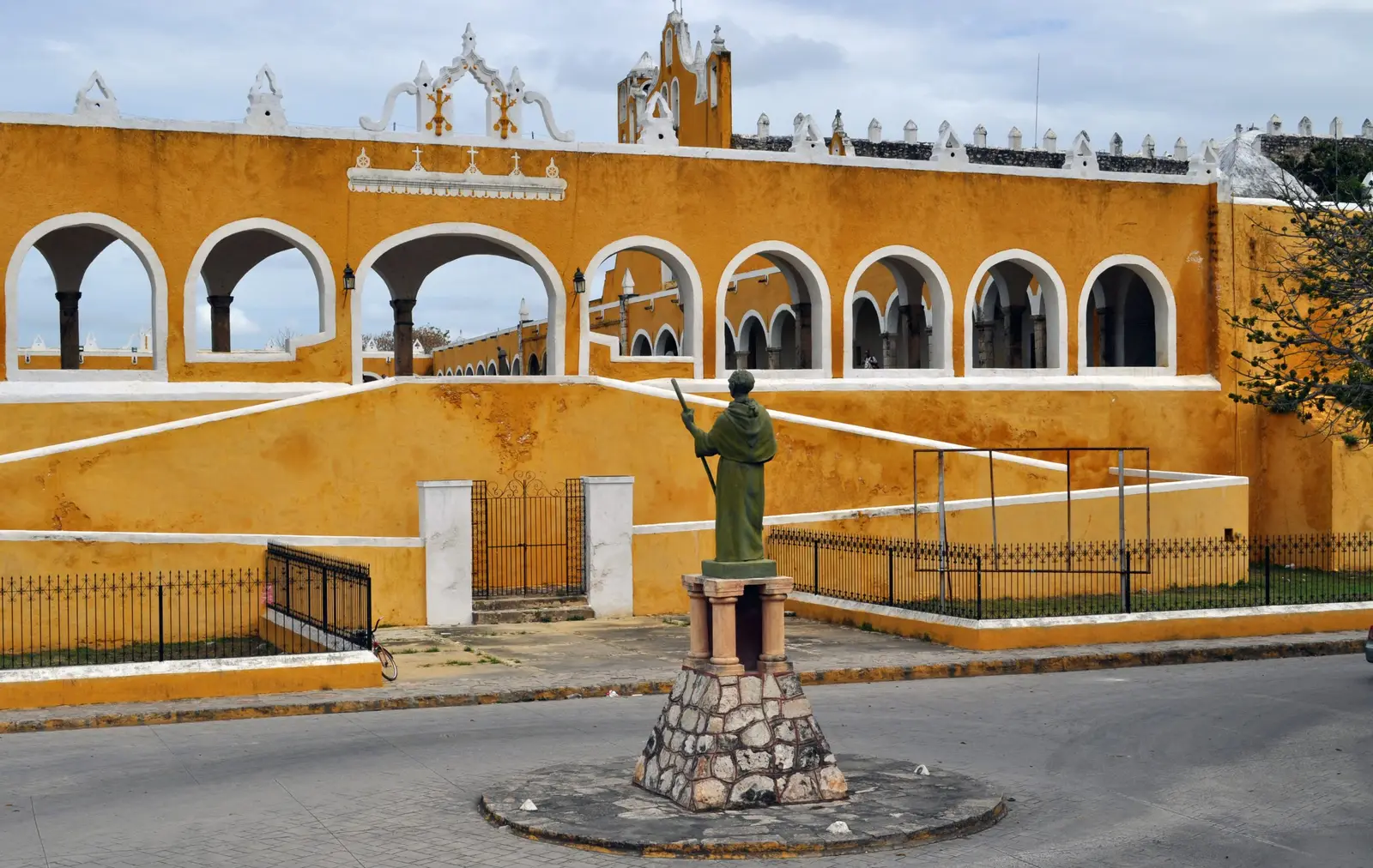 Fachada amarilla con arcadas del convento de Izamal, con la estatua de un fraile al frente