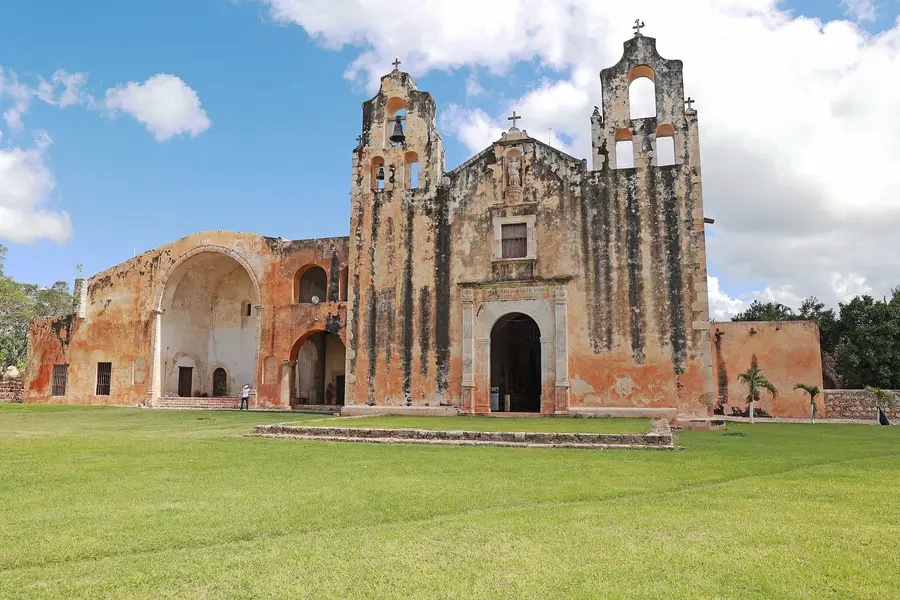 Exconvento de piedra con espadaña, sobre un prado verde, en Maní