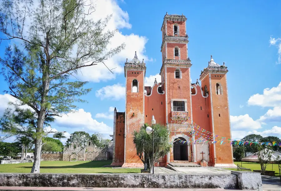 Iglesia anaranjada de tres torres altas bajo cielo azul, en Yaxcabá